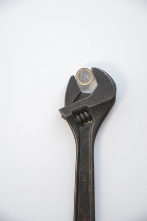Old rusty adjustable wrench with one euro coin on white backgroundの写真素材