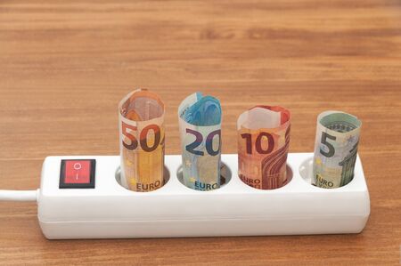 Euro banknotes inserted into an extension socket on a wooden surface. Expensive concepts of energy and cost of electricity. Front view.の写真素材