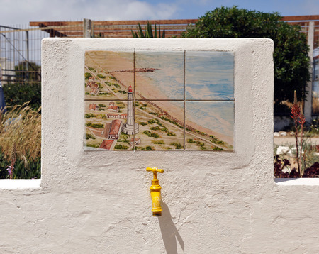Yellow tap with landscape of tiles, whitewashed house, tile of a galleon, Island Culatra, beaches of the Algarve, Portugal, Southern Europeの写真素材