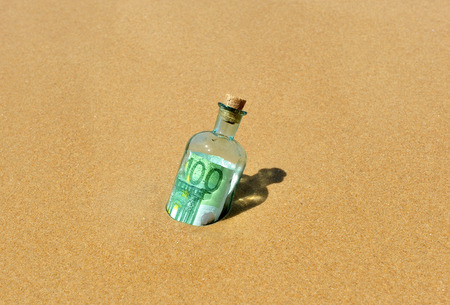 Bottle with 100 euro banknote inside in beach sandの写真素材