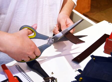 young craftswoman cutting a leather belt with scissors to attach the buckle