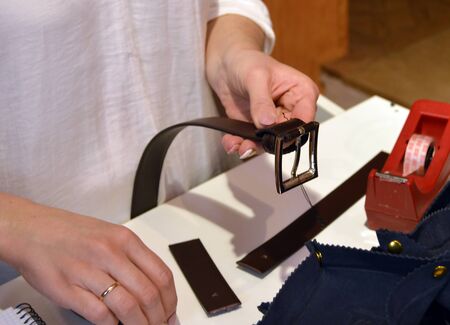 young craftswoman putting the metal buckle on a leather belt