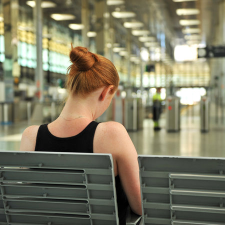 Young redhead woman sitting on a bench and waiting at the modern train station, Cadiz, Andalusia, Spainのeditorial素材