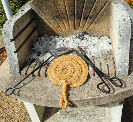 Barbecue utensils, ash catcher, wicker fan and tongs. Concrete grill to prepare a barbecue in the country house gardenの写真素材