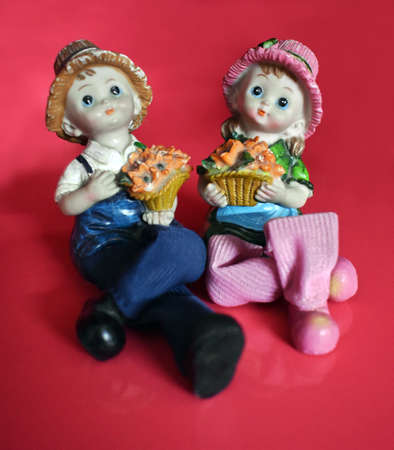 two dolls sitting on a red background with a cupcake in their handsの写真素材