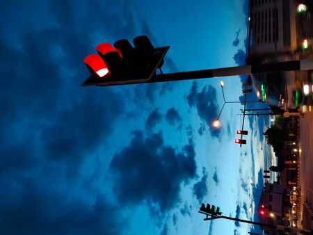 A striking image of a red traffic light against a dramatic dusk sky. The scene captures urban life with vehicles and street elements, showcasing evening ambiance and safety in transportation.の写真素材
