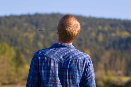 A man with a blue flannel shirt and hay in his mouth looks up and away.の写真素材
