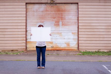 An anonymous girl holds a large white canvas sign with room for text or copy space.の写真素材