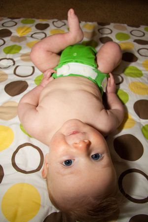 A 3 month old boy lays on a blanket while wearing a green cloth diaper.の写真素材