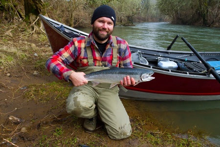 A steelhead fisherman holds his trophy fish by his boat and the river in Oregon.の写真素材