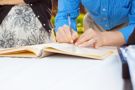 A man and a woman sign a wedding guestbook with a pen.の写真素材