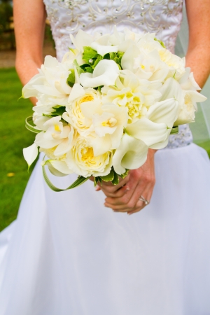 A bride in beautiful white wedding dress holds a bouquet of white and green flowers.の写真素材