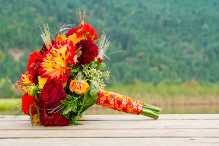 A bride's wedding bouquet sits on a wooden dock with a scenic backdrop of mountains and trees.の写真素材