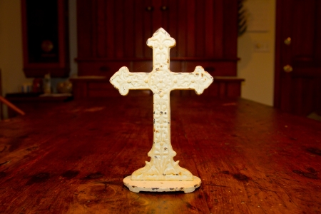 A very old antique white cross photographed on a wood dining table.の写真素材