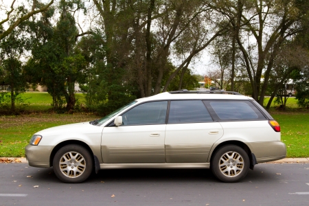 An all wheel drive sport utility wagon parked in front of a park with trees and leaves.の写真素材