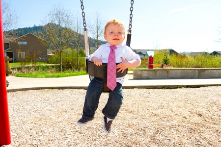 A baby boy plays on a swing set at the park wearing nice clothing.の写真素材