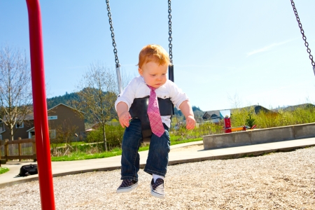 A baby boy plays on a swing set at the park wearing nice clothing.の写真素材