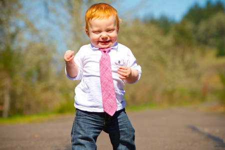 A one year old boy taking some of his first steps outdoors on a path with selective focus while wearing a nice shirt and a necktie.の写真素材