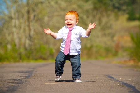 A one year old boy taking some of his first steps outdoors on a path with selective focus while wearing a nice shirt and a necktie.の写真素材