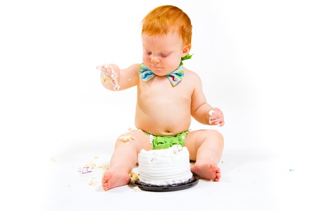 A baby boy gets to eat cake for the first time on his first birthday in this cake smash in studio against a white background.の写真素材