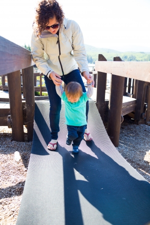 A mom and her son cross an unstable bridge at a playground together.の写真素材