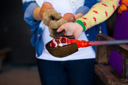A female is blowing glass and using a wooden shaping tool to form the shape she wants the glass to end up as. The glass is hot and molten so she has to use water with the wood.の写真素材