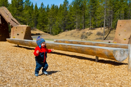 A one-year-old boy plays at a park outdoors with wood chips and structures to keep him entertained.の写真素材