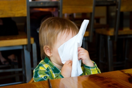 A young one year old toddler boy plays with a napkin at a restaurant while waiting for his food.の写真素材