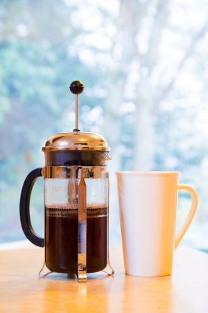 Coffee is being made in a french press along with cream and sugar on the kitchen counter early in the morning.の写真素材