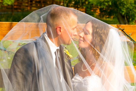 Bridal veil covers the bride and groom on their wedding day while they share a special moment together for a portrait of their love.の写真素材