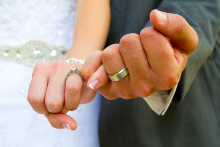 Bride and groom with their hands together and their pinky fingers interlocked for this unique color image of their hands and wedding rings.の写真素材