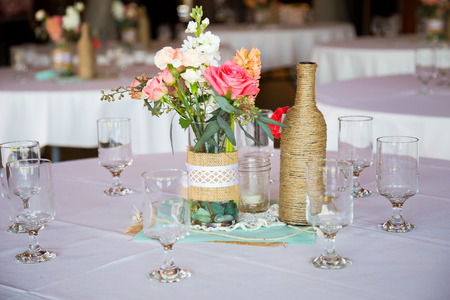 DIY wedding decor table centerpieces with wine bottles wrapped in burlap twine and rose flowers.の写真素材