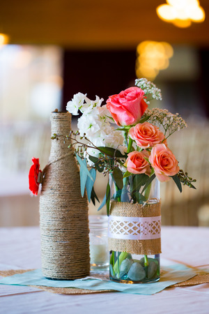 DIY wedding decor table centerpieces with wine bottles wrapped in burlap twine and rose flowers.の写真素材