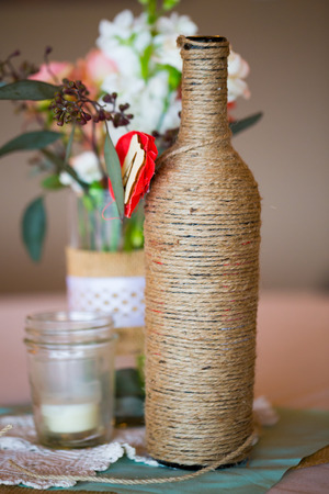 DIY wedding decor table centerpieces with wine bottles wrapped in burlap twine and rose flowers.の写真素材