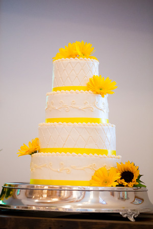 Tall four tiered wedding cake at a reception with yellow and white.の写真素材