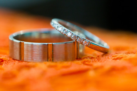 Bride and groom wedding rings photographed before the ceremony on an orange tablecloth.