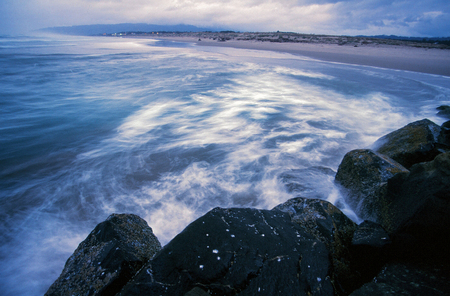 Waves crash next to a jetty as the tide rolls in on an Oregon Beach in the Winter.
