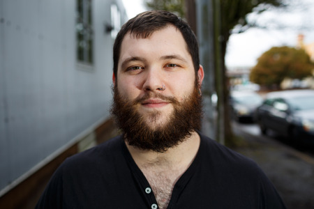 Young adult man outdoors in an urban environment for a lifestyle portrait of a bearded hipster.