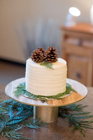 White wedding cake at a reception with a pinecone topper.