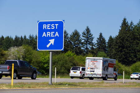 INTERSTATE 5, OR - MAY 7, 2015: Blue rest area sign point to a public exit off the highway with vehicles passing by in the background.のeditorial素材
