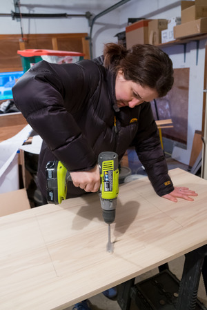 SPRINGFIELD, OR - JANUARY 31, 2017: Female construction worker using a driver to drill a hole through a wood vanity top on a major DIY house renovation and remodel project.のeditorial素材