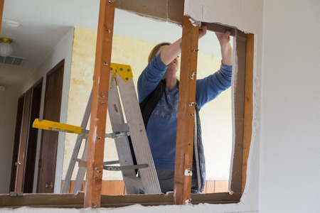 SPRINGFIELD, OR - DECEMBER 20, 2017: Female construction worker and homeowner using a sawsall tool to cut drywall out and take a wall down to a half-wall during a DIY house renovation.のeditorial素材