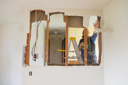 SPRINGFIELD, OR - DECEMBER 20, 2017: Female construction worker and homeowner using a sawsall tool to cut drywall out and take a wall down to a half-wall during a DIY house renovation.のeditorial素材