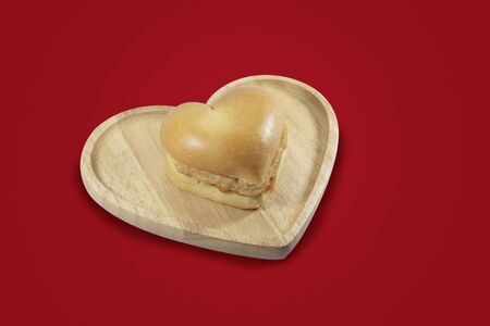 Heart shape hamburger in a brown heart shape wooden plate isolate on red background  . Top view, close up. Love burger fast food concept with copy space.のイラスト素材