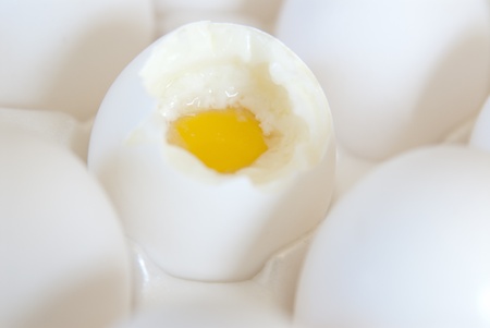 A bunch of white eggs in a white crete and one is open and half cooked.の写真素材