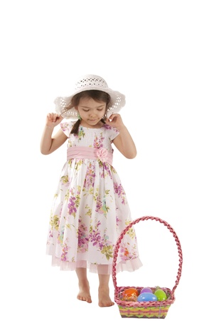 This is a little girl wearing a white dress ans hat playing Easter eggs hunt.の写真素材