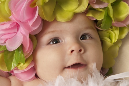 This is a close-up of a little baby girl laying down over a beige blanket and wearing a flower crown の写真素材