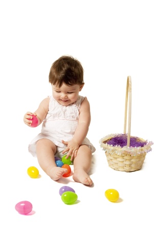 This is a little baby girl with a dress playing with eggs for Easter isolated on a white background.の写真素材