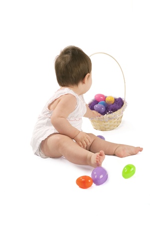 This is a little baby girl with a white dress playing with eggs for Easter isolated on a white background.の写真素材