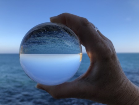Woman's hand holding a crystal ball, looking through to the ocean and sky. Creative photography, crystal ball refractionの写真素材